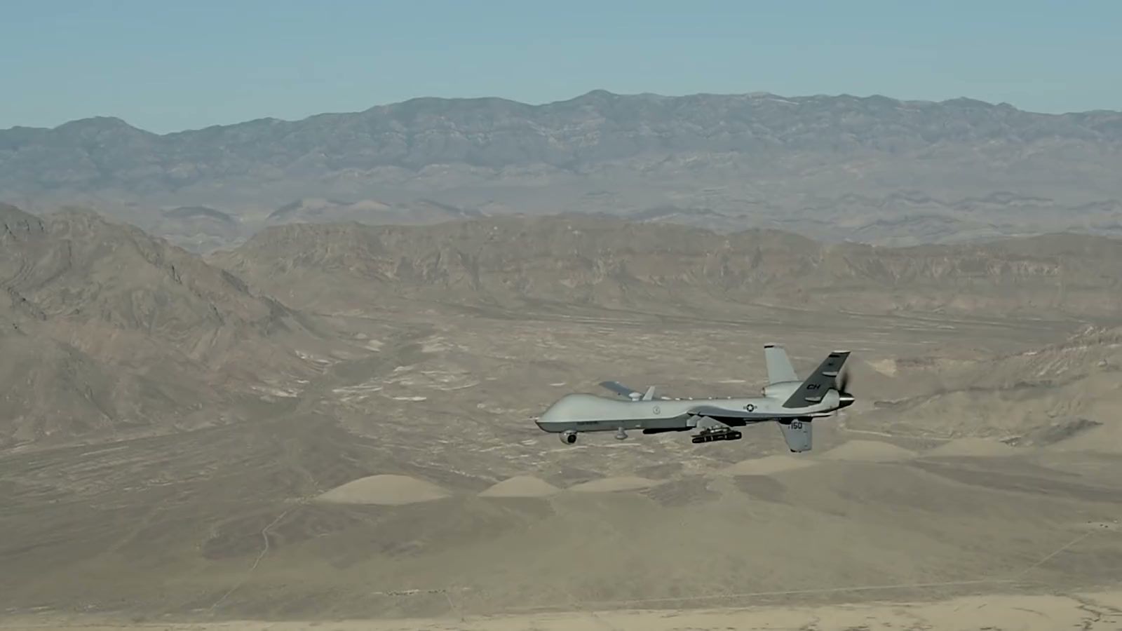 An MQ-9 military unmanned aircraft flying over desert mountains during a training flight.